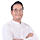 Seorang pria tersenyum dengan lengan disilangkan, mengenakan kemeja putih. Latar belakang berwarna polos, menciptakan kesan profesional dan bersahabat.