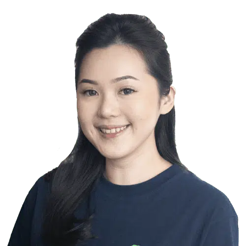 Seorang wanita dengan rambut panjang mengenakan kaus gelap, berdiri di latar belakang hijau yang tanpa detail tambahan, memberikan kesan fokus pada sosoknya.