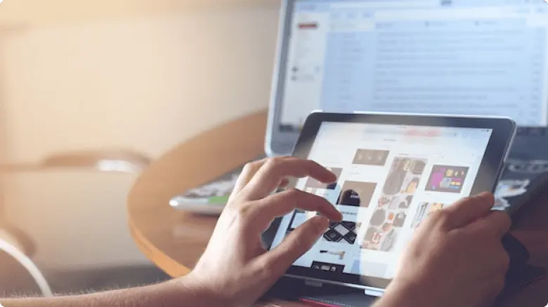 Sebuah tablet digunakan untuk menelusuri berbagai gambar dan desain, terletak di meja yang berdekatan dengan laptop, menciptakan lingkungan kerja.