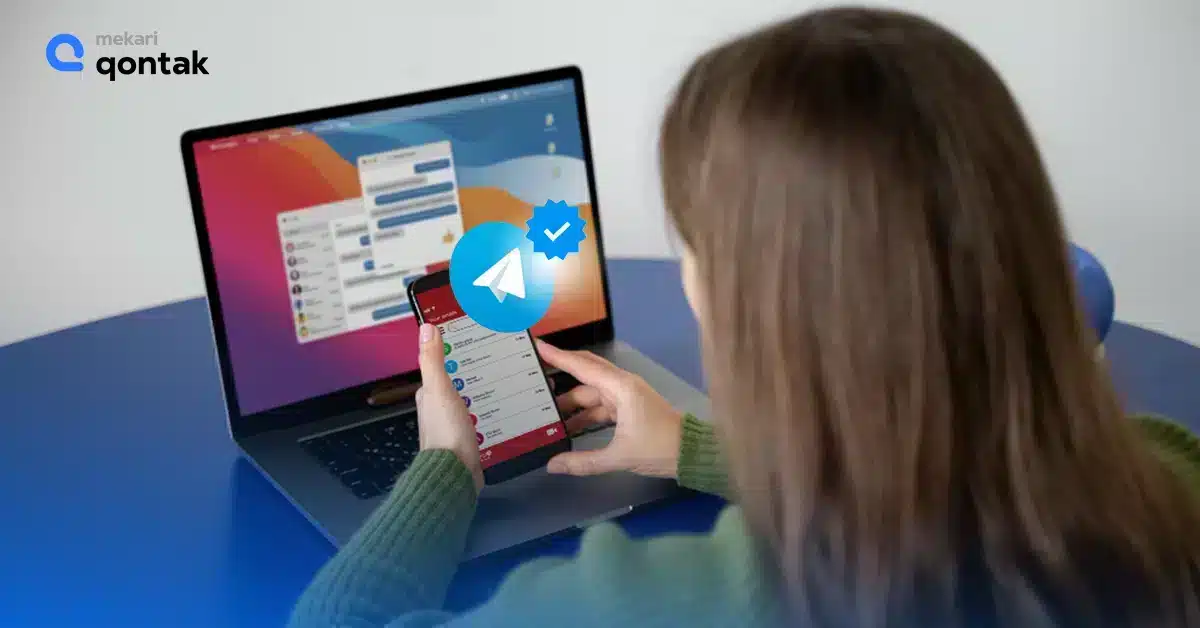 Seorang pengguna memeriksa aplikasi di ponsel sambil duduk di depan laptop, mengelola pesan dengan interface interaktif. Latar belakang minimalis meningkatkan fokus pada aktivitas.