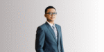 Pria mengenakan jas formal berwarna biru, berdiri tegak di depan latar belakang gradasi abu-abu, menciptakan kesan profesional dan elegan.