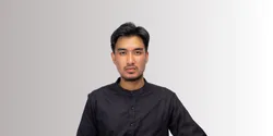 Seorang pria mengenakan pakaian hitam duduk dengan tenang di depan latar belakang berwarna abu-abu. Suasana tampak formal dan profesional.